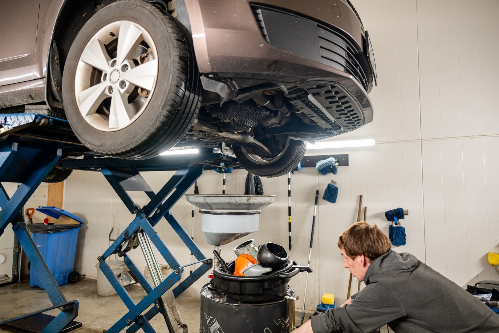 A mechanic working under a car raised on a lift, performing service.