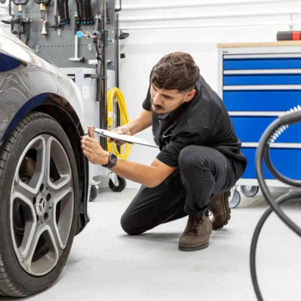 Auto body technician inspecting a vehicle panel and wheel area, representing the professional evaluation to look for when choosing a body shop.