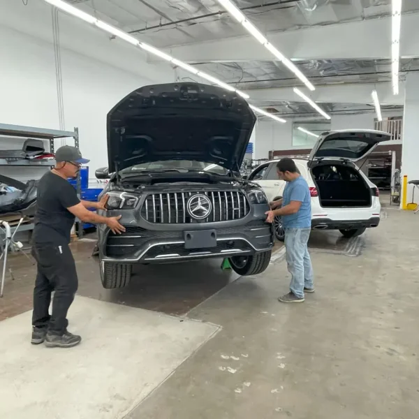 Technicians inspecting a Mercedes SUV at an auto body shop while evaluating collision damage and comparing repair needs with an insurance estimate.