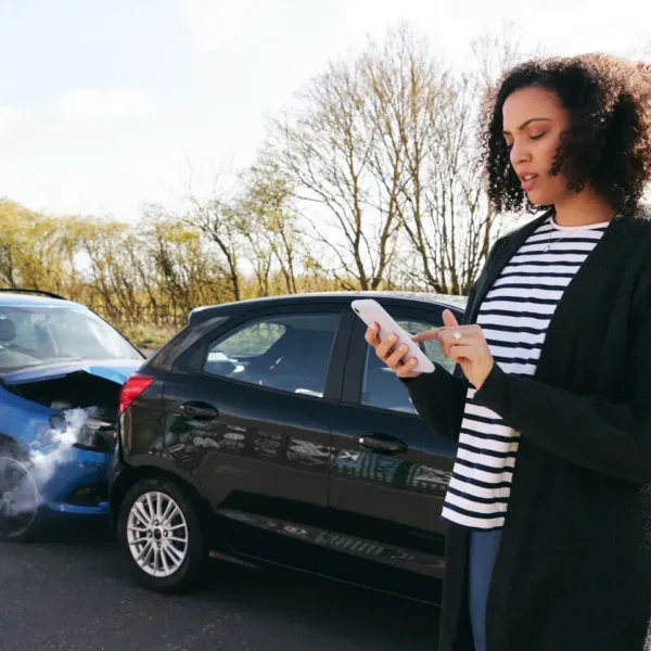 Driver using a phone beside a damaged car after a crash, illustrating how an auto body shop supports vehicle safety and collision repair.