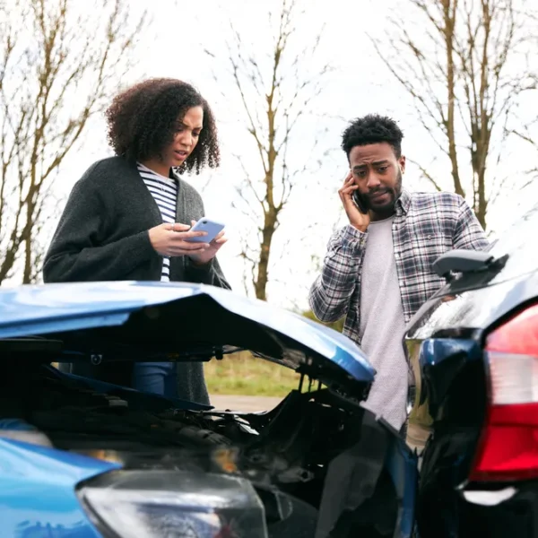 Two drivers standing beside damaged vehicles after a collision, reviewing the scene and contacting help before arranging auto body repair.