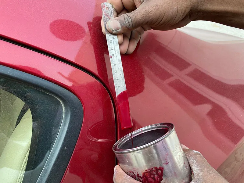Technician comparing red automotive paint to a vehicle panel for precise auto color matching and seamless collision repair refinishing.